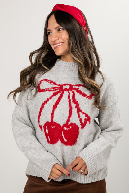 Woman wearing a gray sweater with red cherry design and a red headband against a white background