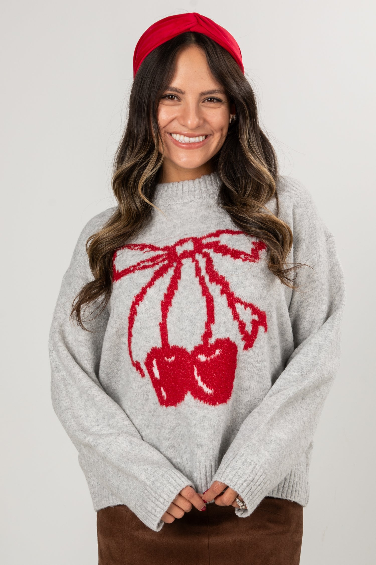 Woman wearing a gray sweater with a red bow design and a red headband against a white background