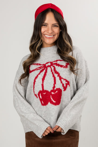 Woman wearing a gray sweater with a red bow design and a red headband against a white background