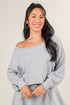 Woman wearing a gray off-shoulder sweater against a plain background