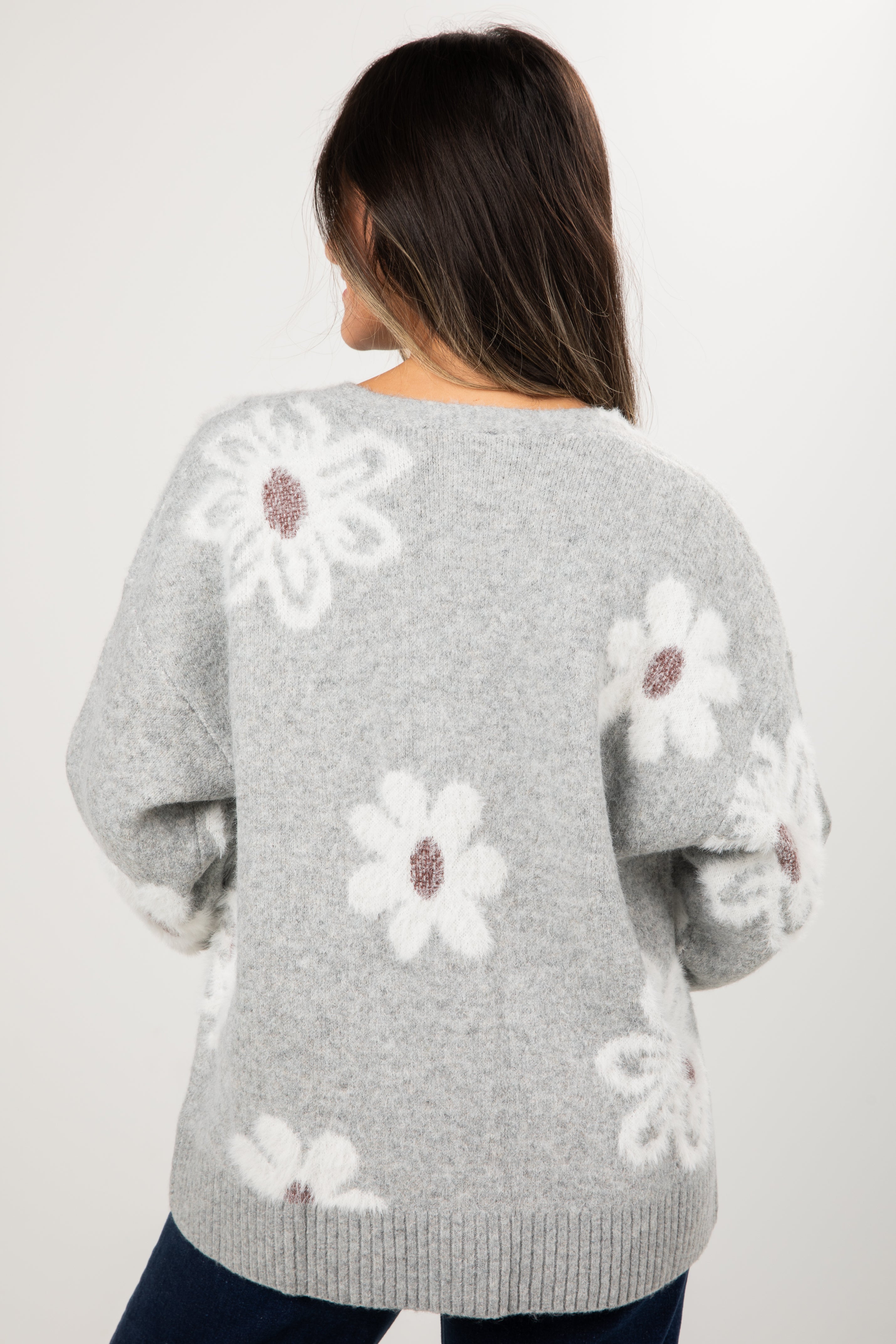Gray sweater with white floral patterns worn by a person on a plain background