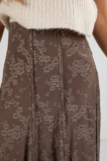 Brown floral-patterned pants worn with a white top on a white background