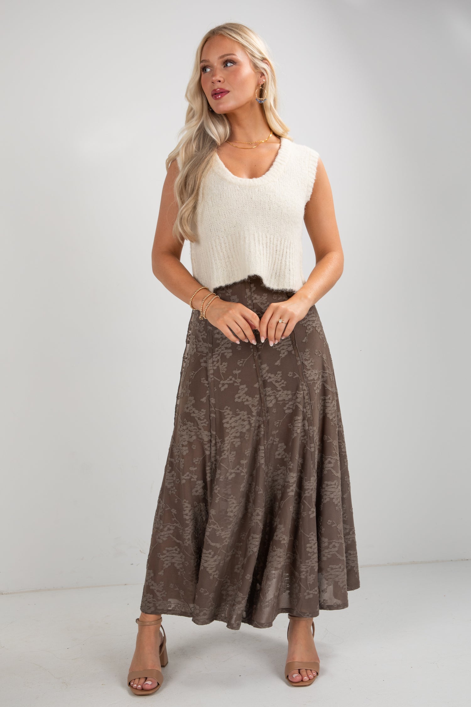 Woman wearing a white sleeveless top and brown patterned skirt on a plain background