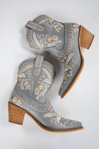 Gray embroidered cowboy boots with brown block heels on a light gray background