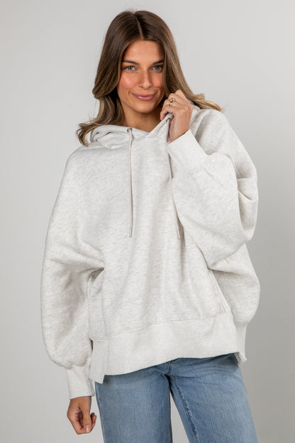 Woman wearing a light gray hoodie and blue jeans on a plain background
