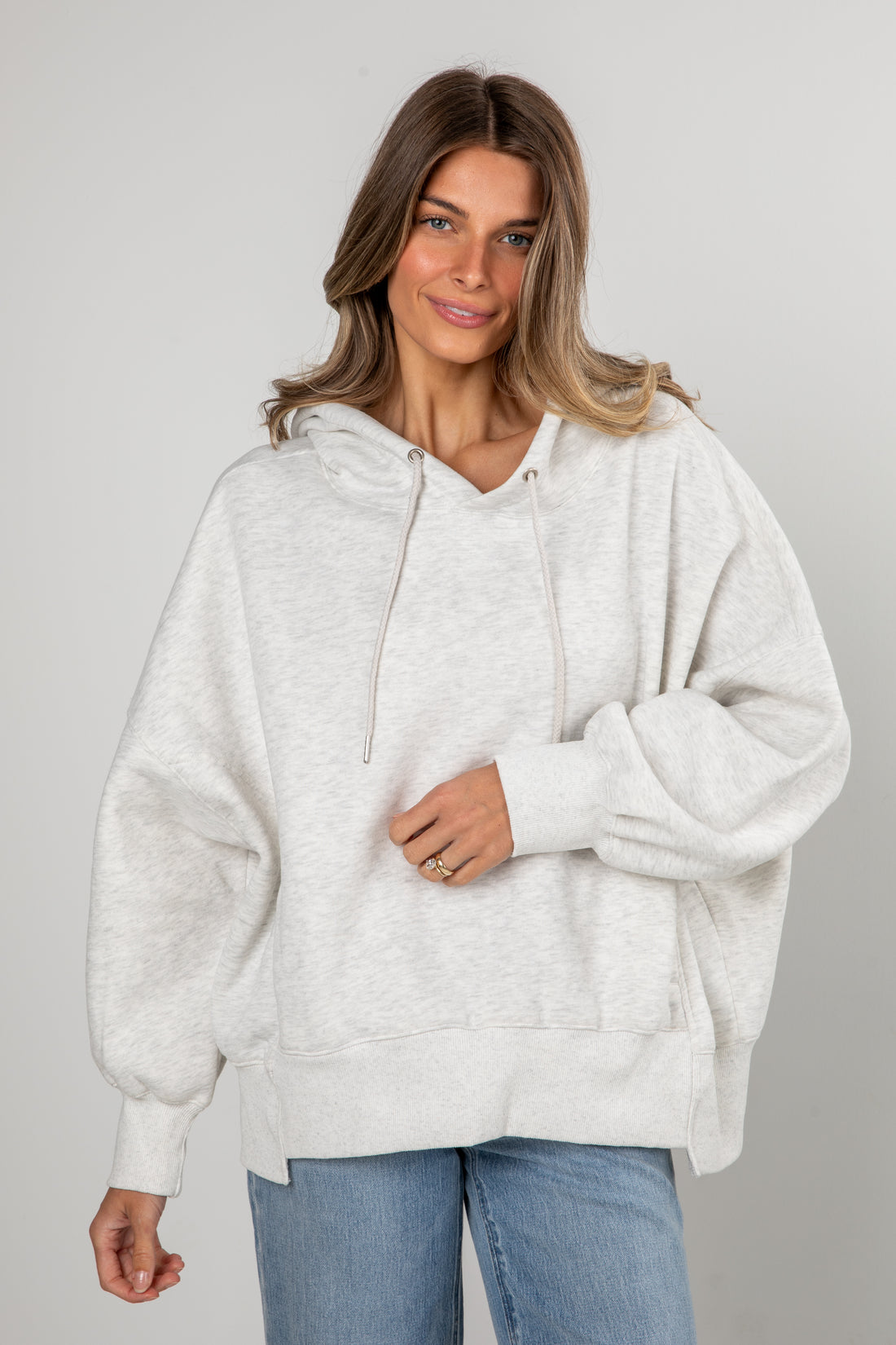Woman wearing a light gray hoodie and blue jeans on a plain background