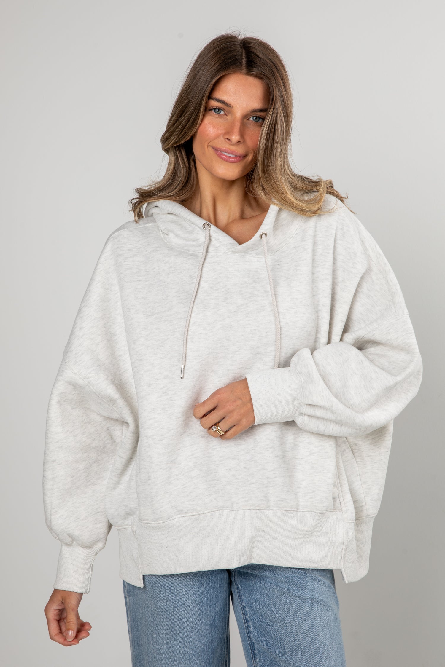 Woman wearing a light gray hoodie and blue jeans on a plain background