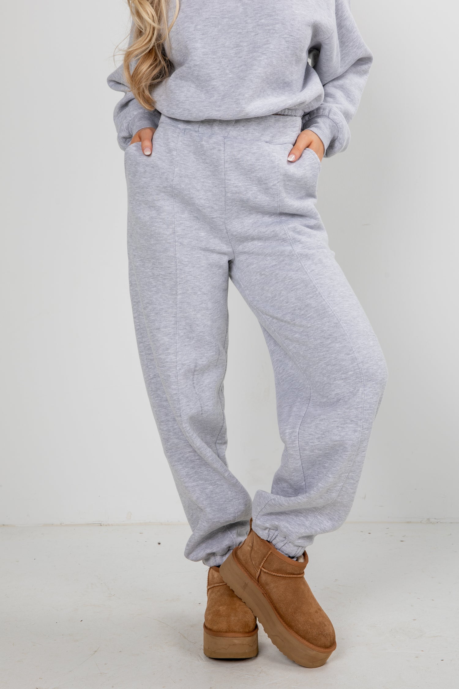 Person wearing a gray sweatshirt and pants with brown boots on a white background