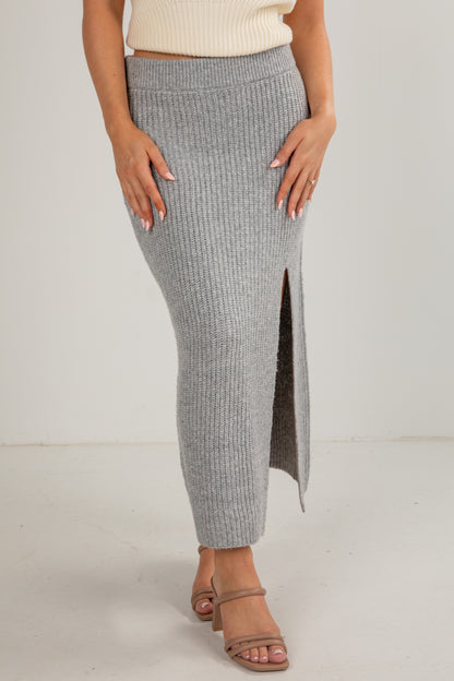 Person wearing a gray ribbed skirt with a white top on a plain background