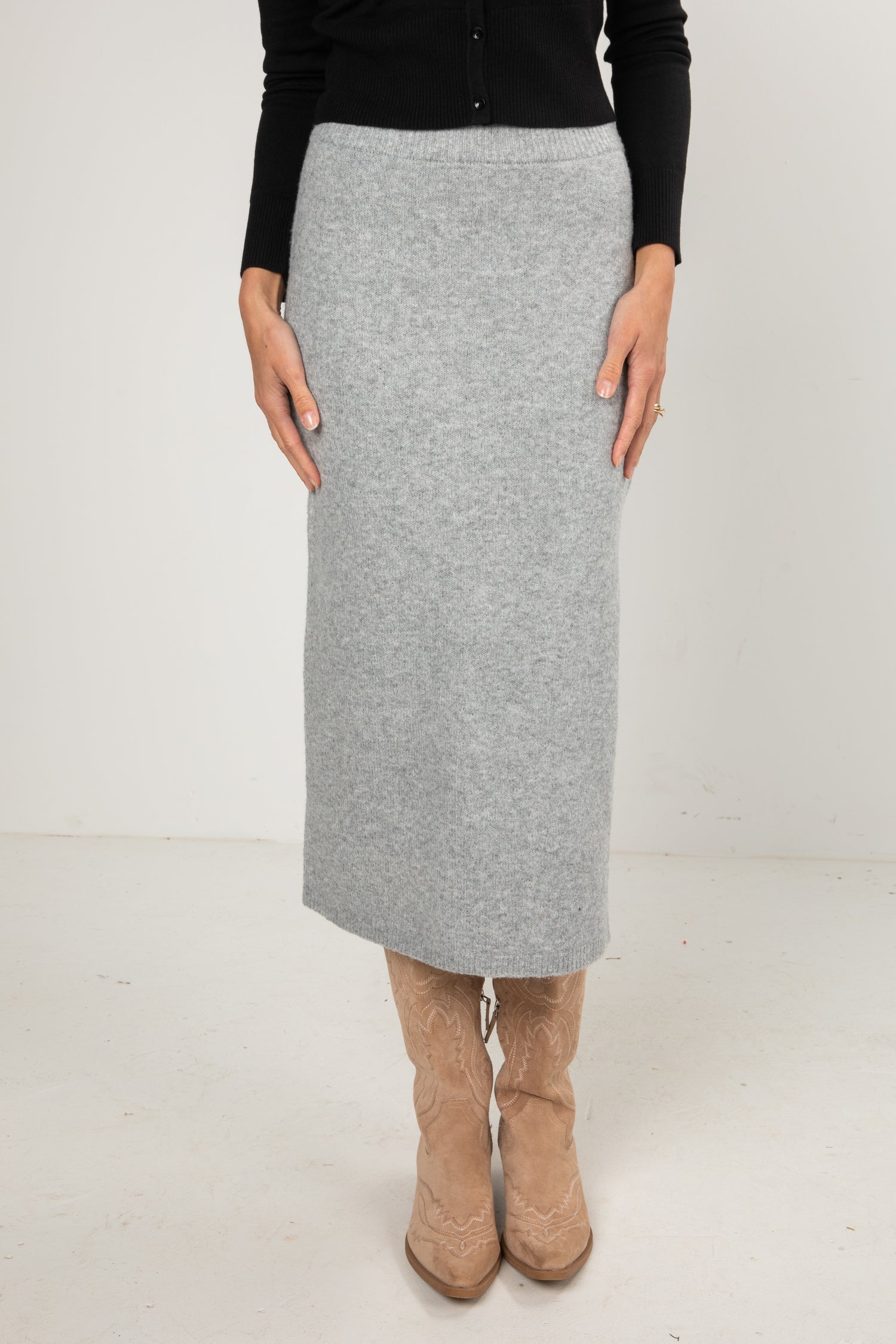 Woman wearing a black button-down cardigan and a grey knit midi skirt styled with tan cowboy boots.