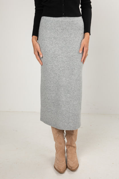 Woman wearing a black button-down cardigan and a grey knit midi skirt styled with tan cowboy boots.
