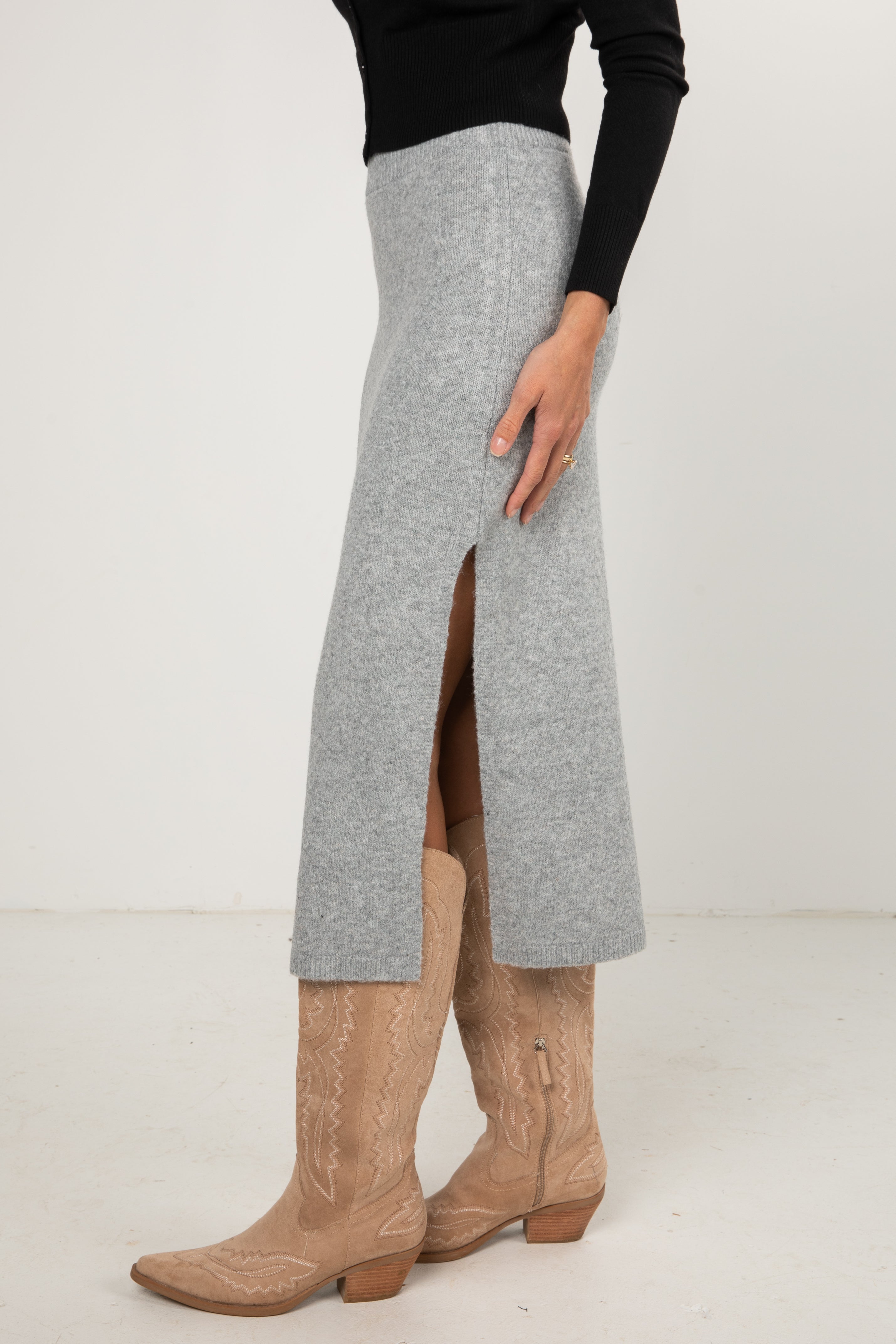 Woman wearing a black button-down cardigan and a grey knit midi skirt styled with tan cowboy boots.