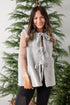 Woman wearing a gray knitted vest with a Christmas tree in the background