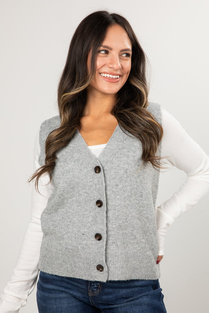 Woman wearing a gray cardigan vest with buttons on a plain background