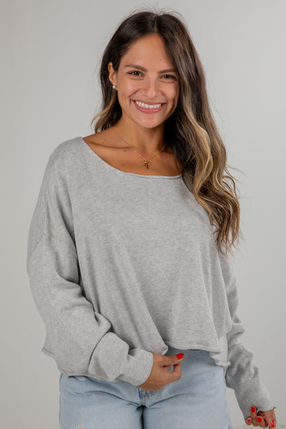 Woman wearing a gray sweater and light blue jeans against a plain background