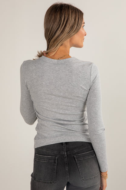 Woman wearing a gray long-sleeve top and dark jeans against a plain background