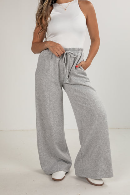 Person wearing gray wide-leg pants and a white top on a plain background