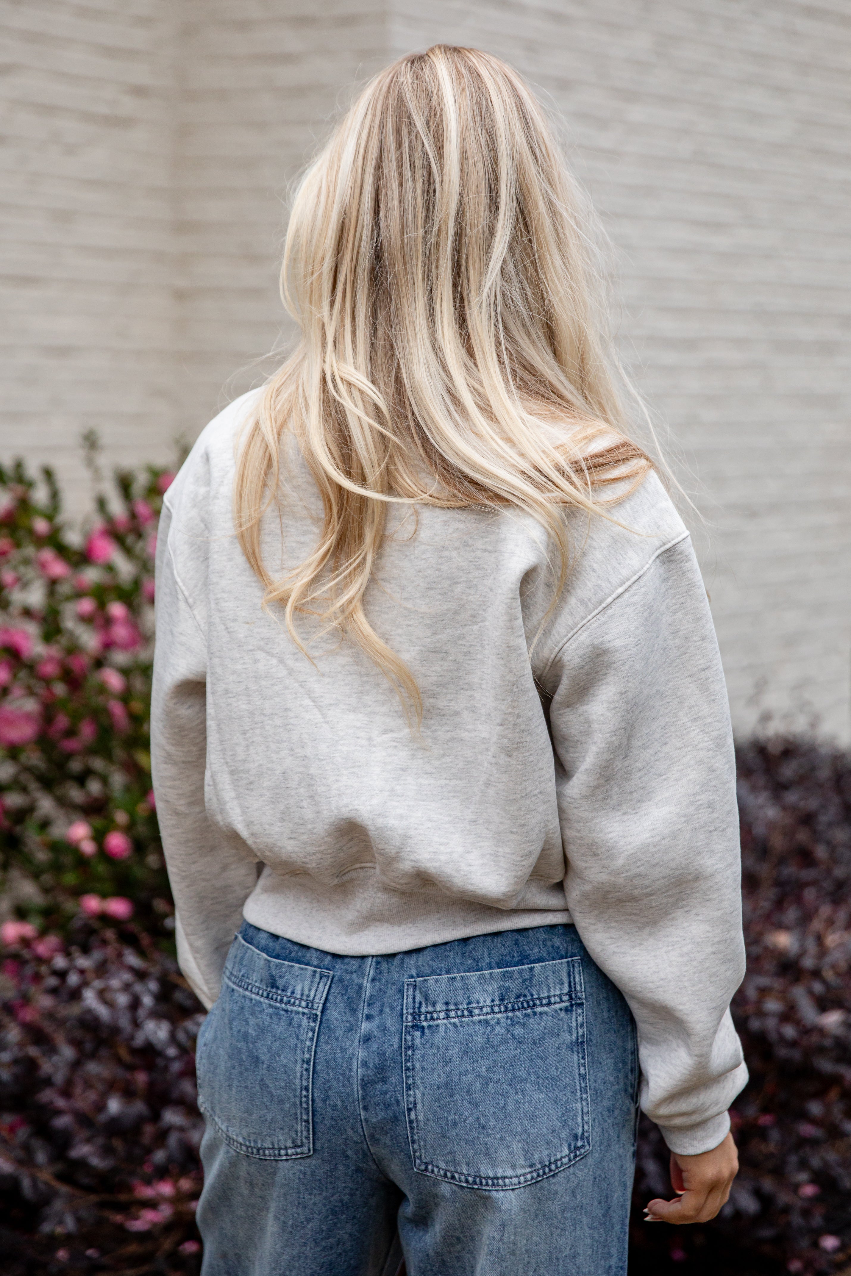 Person wearing a light gray sweatshirt and blue jeans with a blurred background