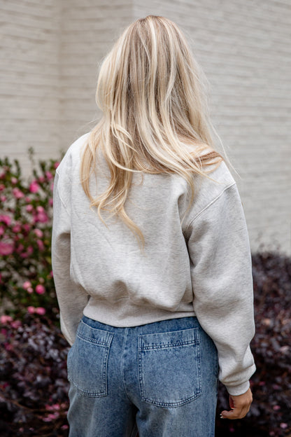 Person wearing a light gray sweatshirt and blue jeans with a blurred background