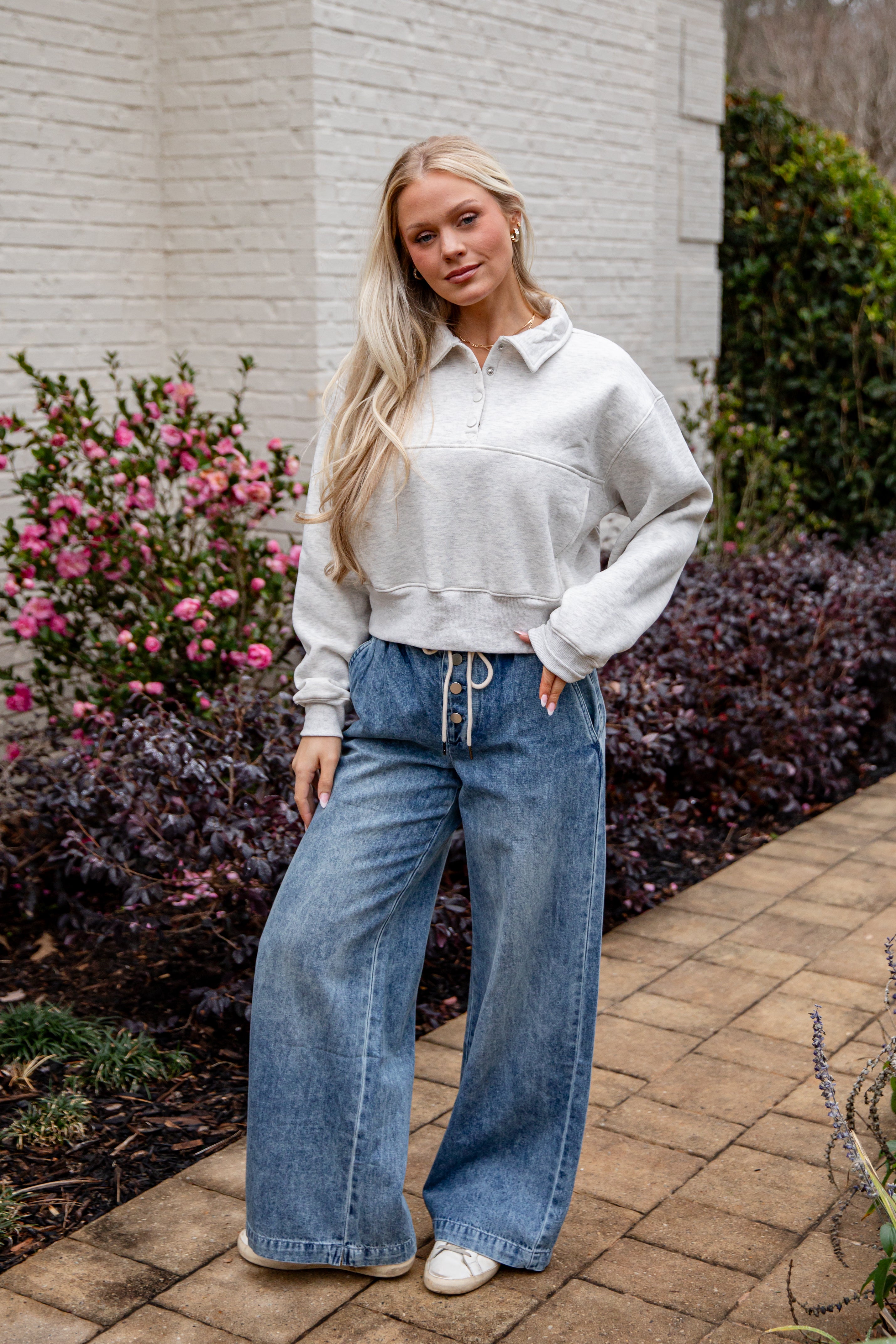 Woman wearing a light gray sweater and blue jeans standing outdoors.