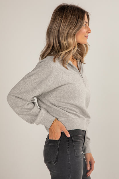 Woman wearing a gray sweater and dark jeans against a plain background