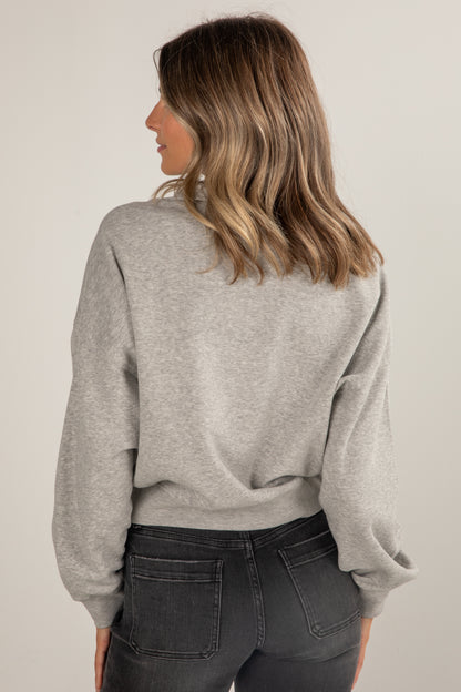 Woman wearing a gray sweater and dark jeans against a plain background