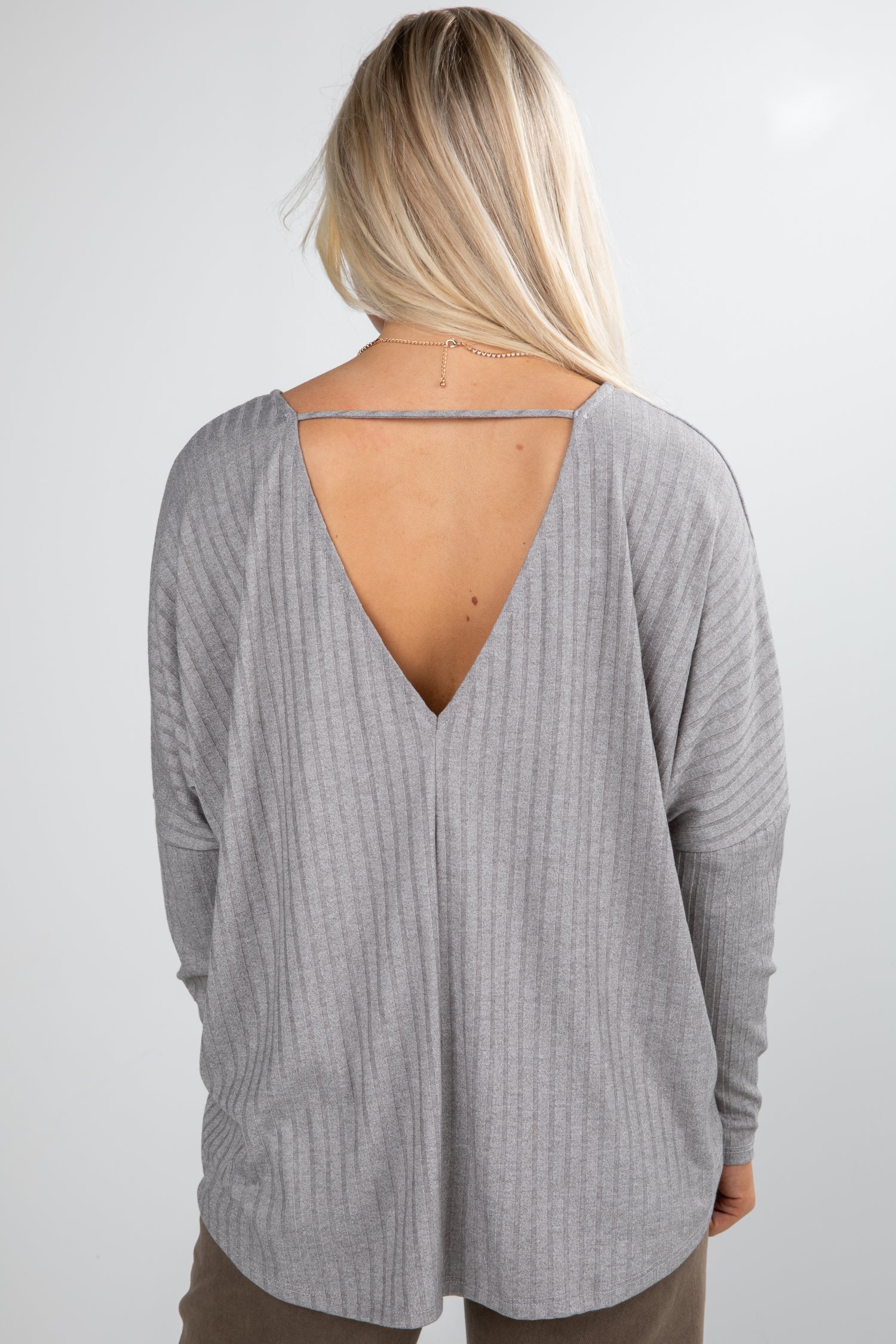 Person wearing a gray long-sleeve top with an open back on a white background