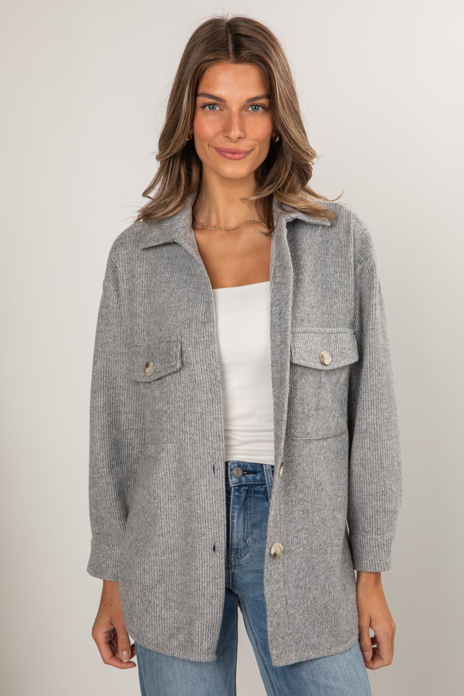 Woman wearing a gray coat over a white top and blue jeans on a plain background