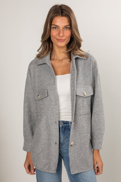 Woman wearing a gray coat over a white top and blue jeans on a plain background