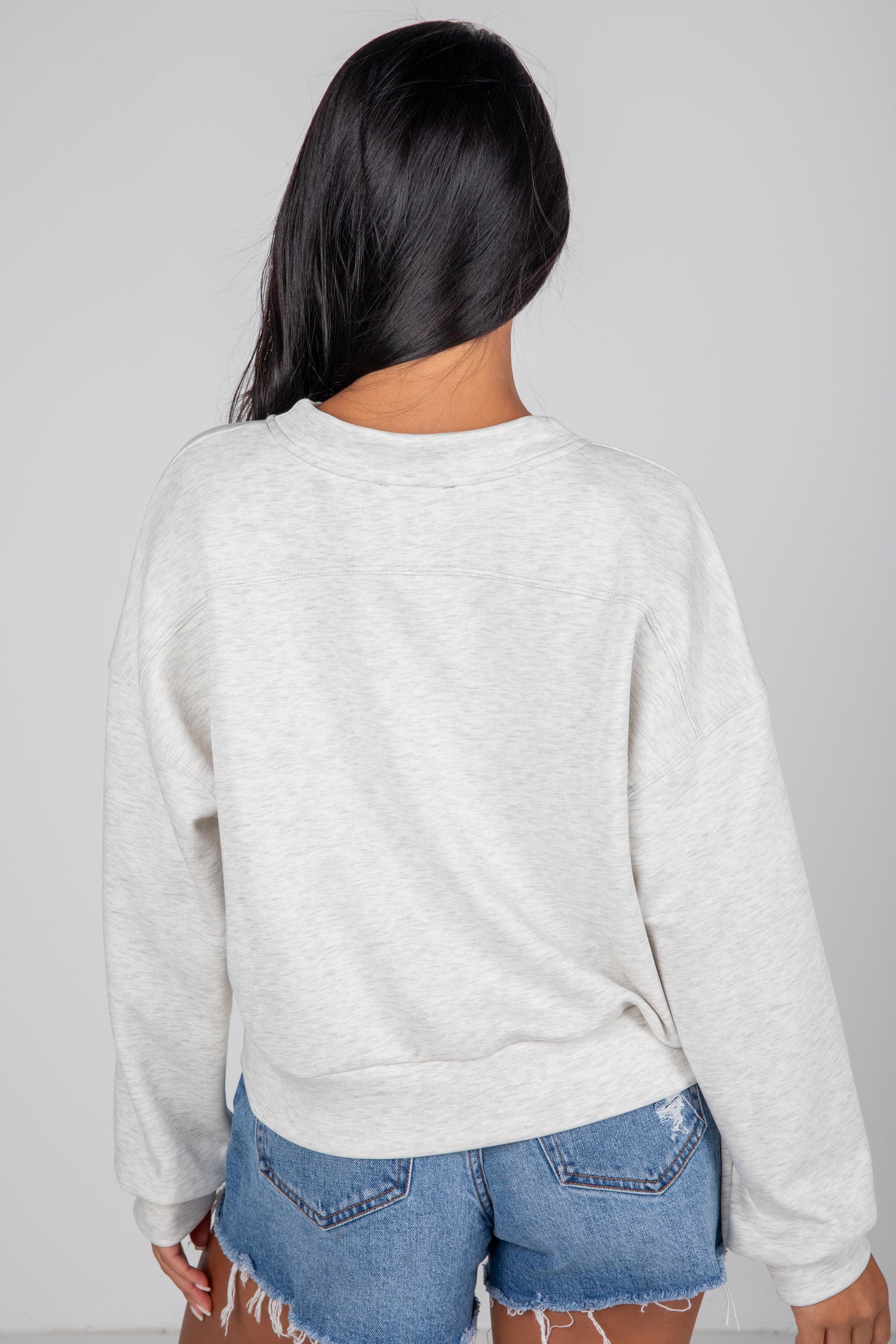 Person wearing a light gray sweatshirt and blue jeans on a plain background