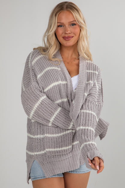 Woman wearing a gray and white striped cardigan on a plain background