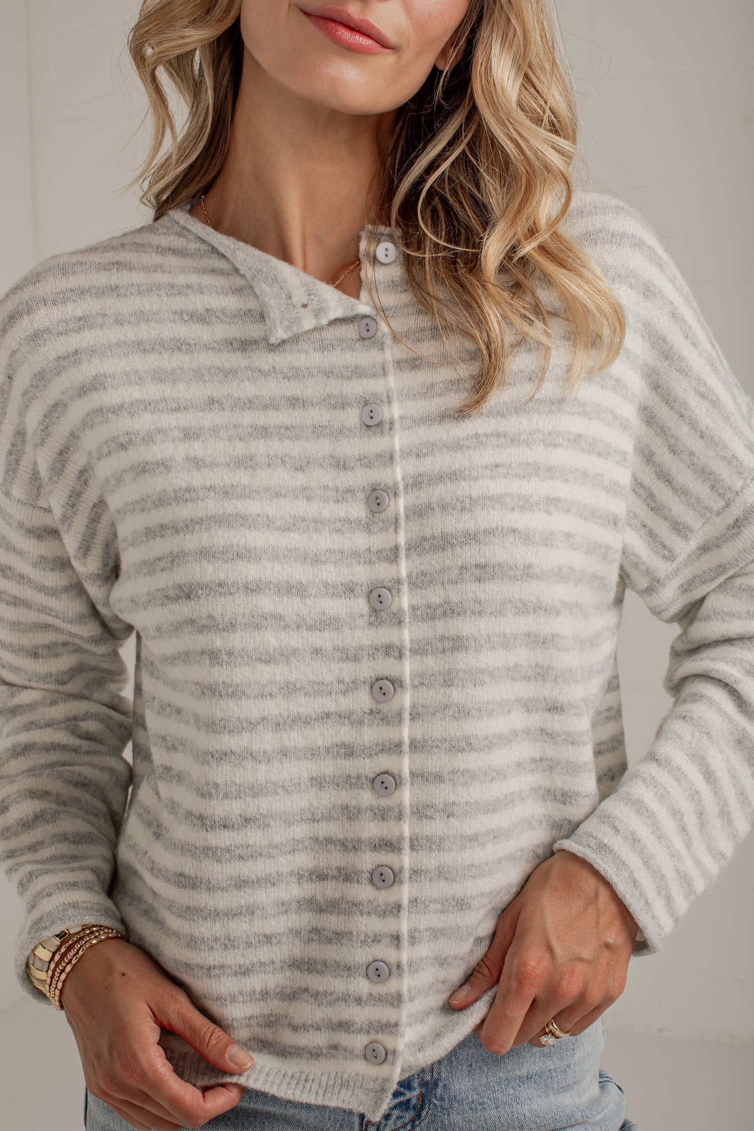 A woman wearing a light gray and white striped knit cardigan sweater with a button-down front and a small folded collar, paired with light blue jeans.