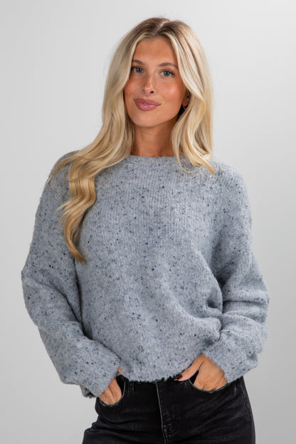 Woman wearing a gray speckled sweater against a plain background