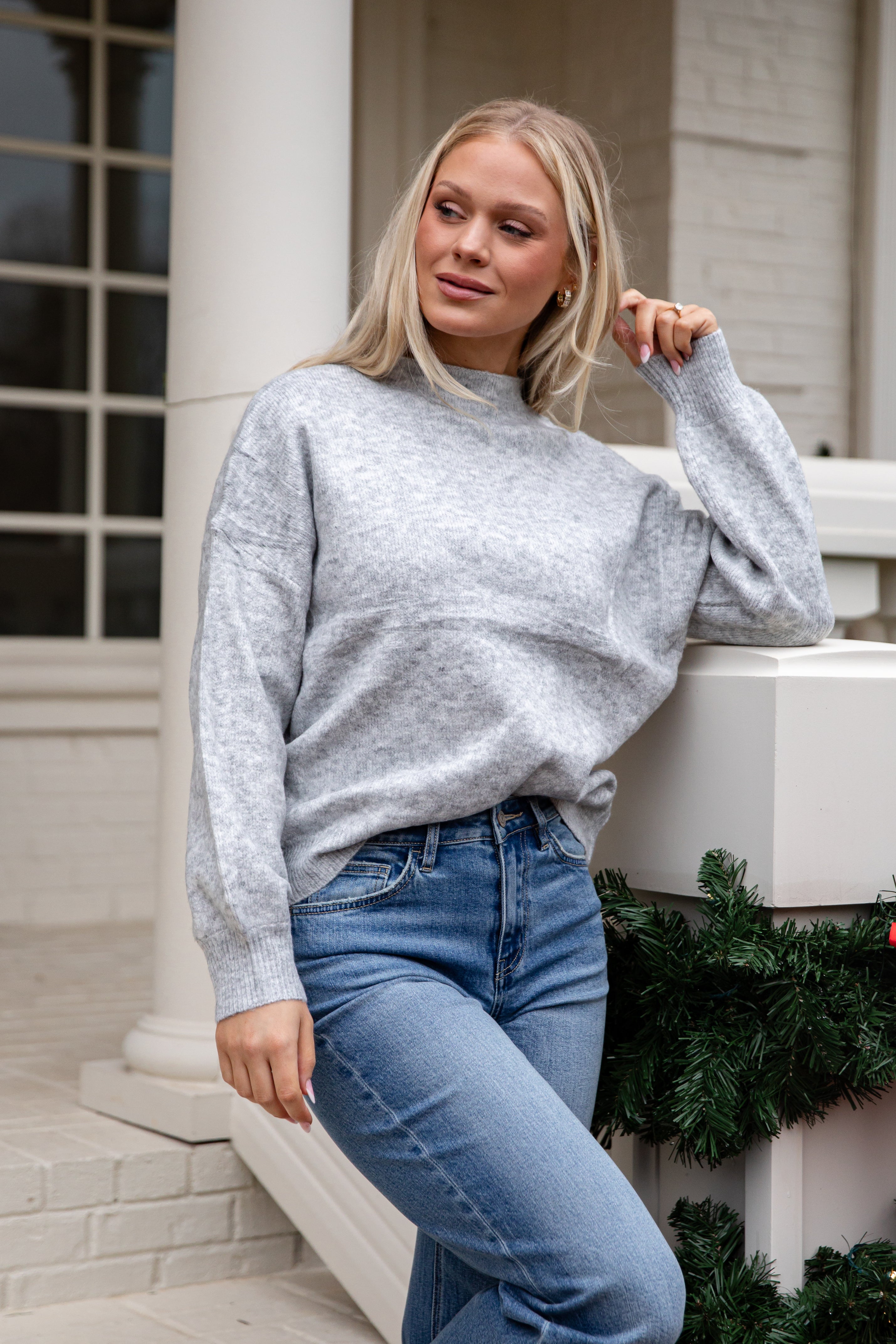 Woman wearing a gray sweater and blue jeans standing on steps with a decorative background