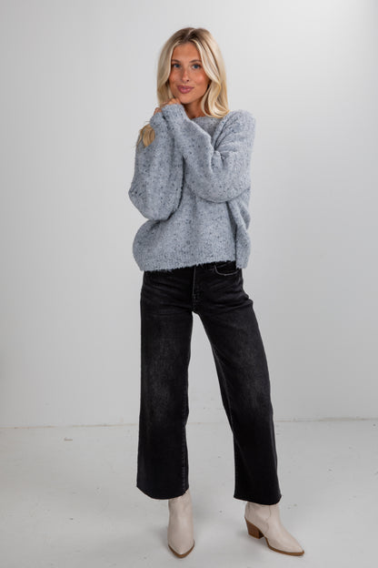 Woman wearing a gray sweater, black jeans, and white boots on a white background