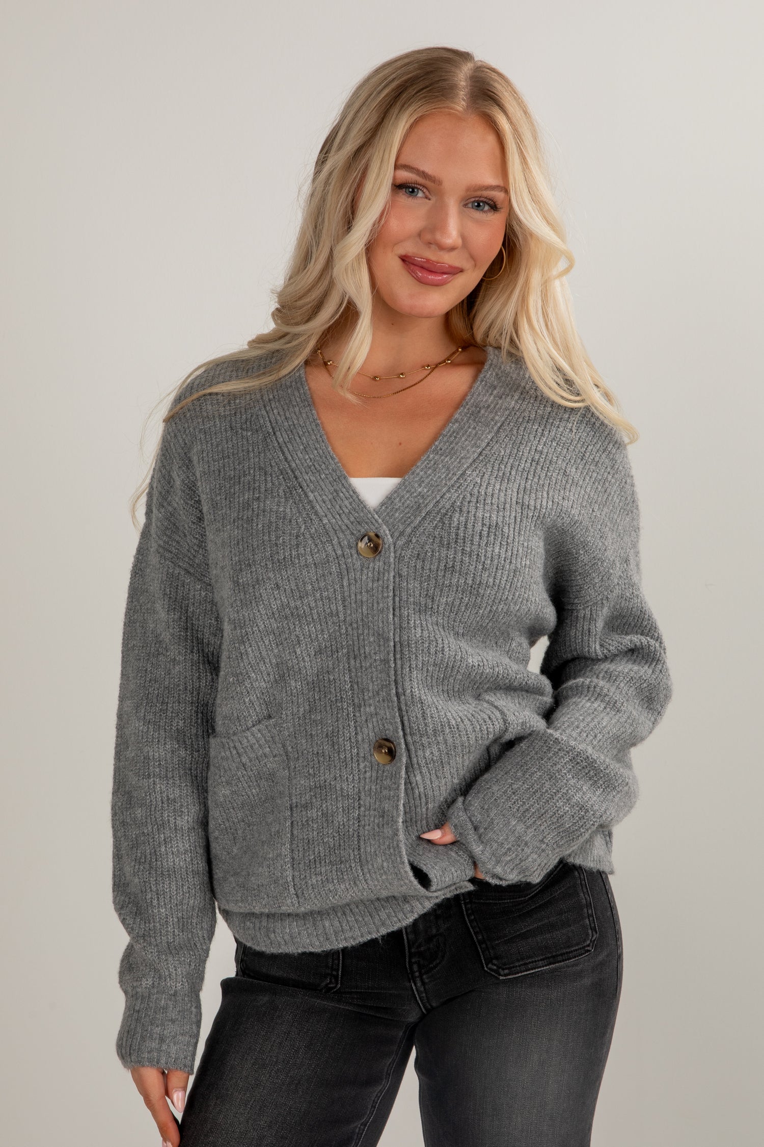 Woman wearing a gray cardigan with buttons on a plain background