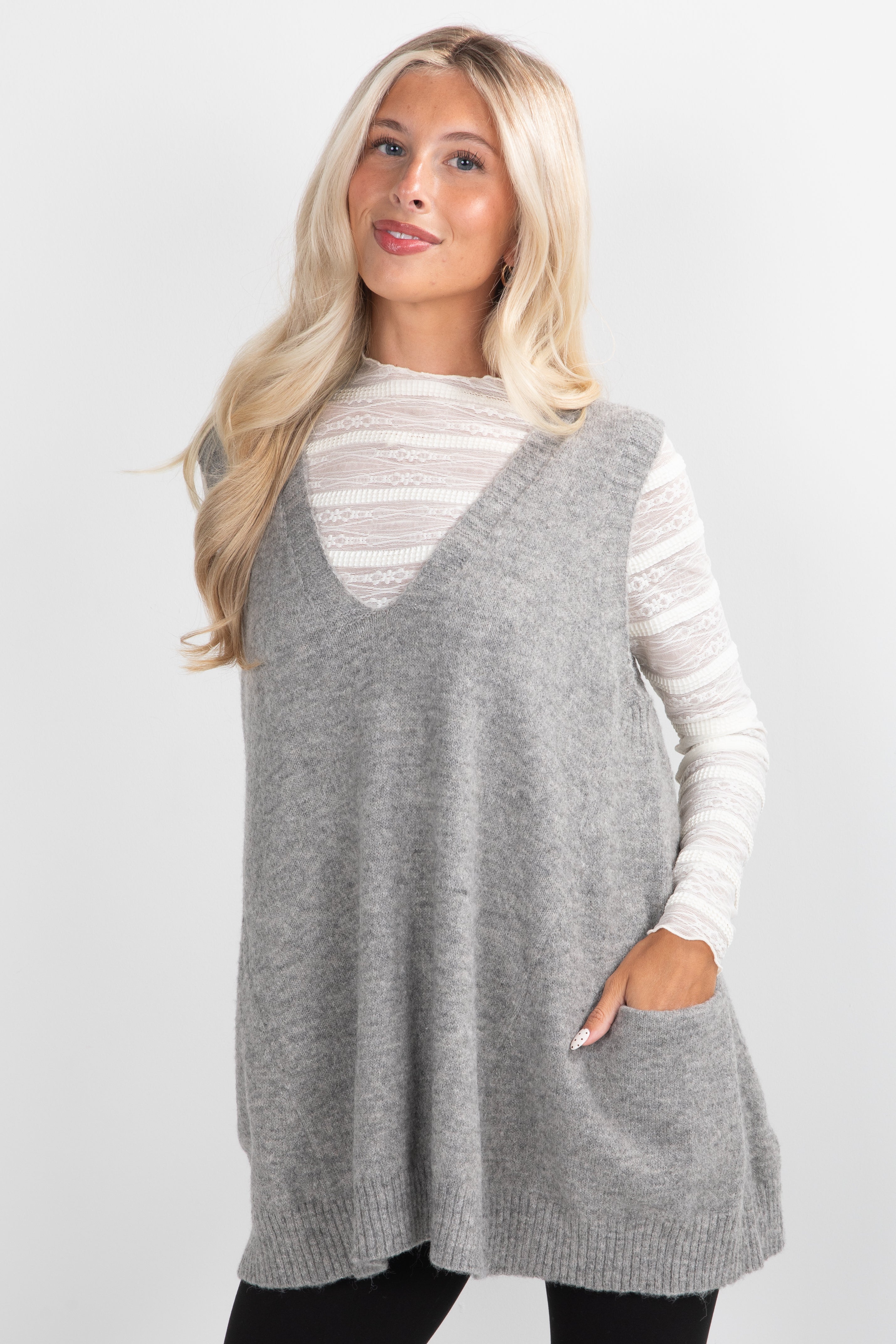 Woman wearing a gray sleeveless sweater over a white shirt on a plain background