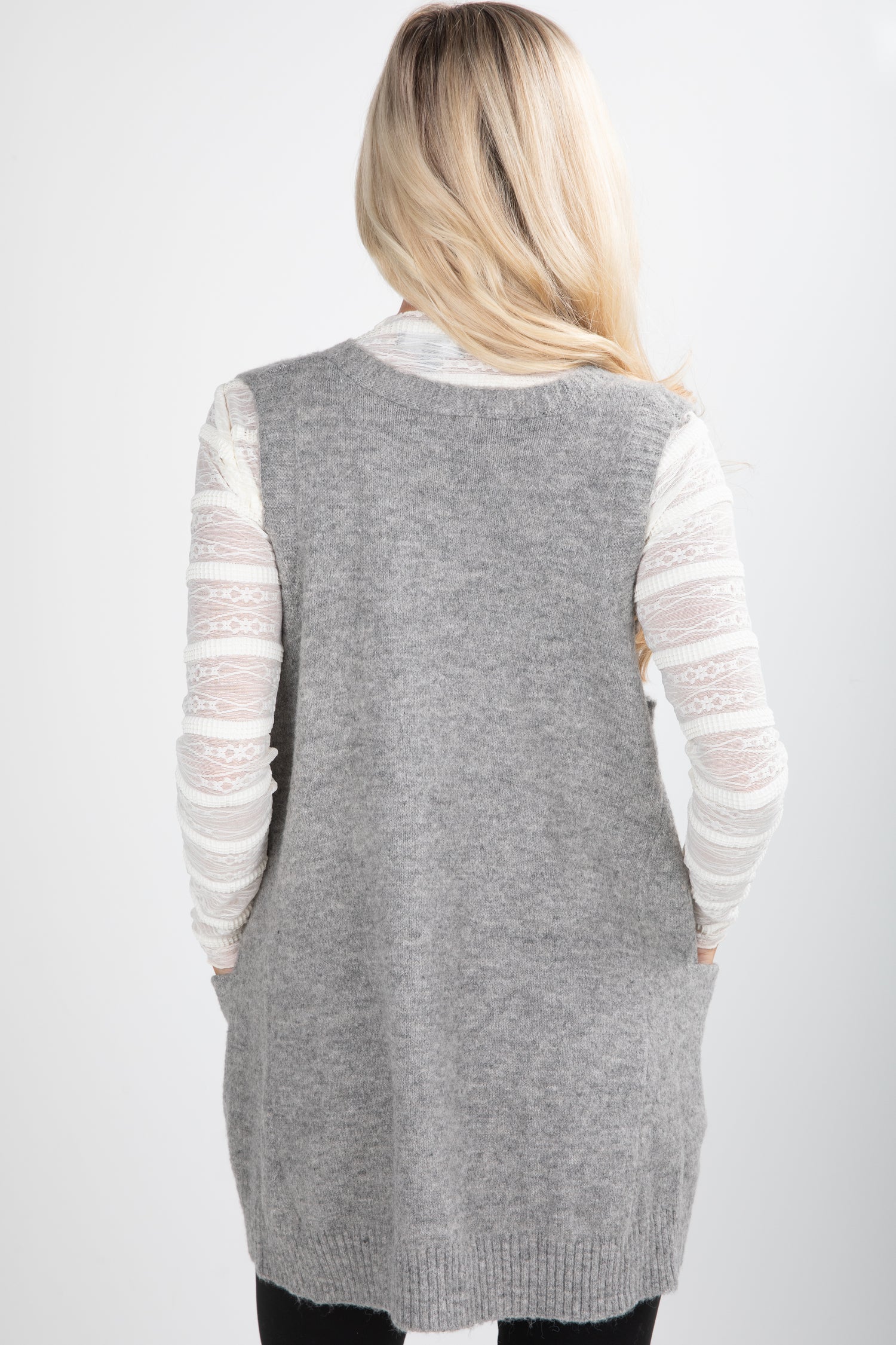 Person wearing a gray cardigan over a white long-sleeve shirt on a white background