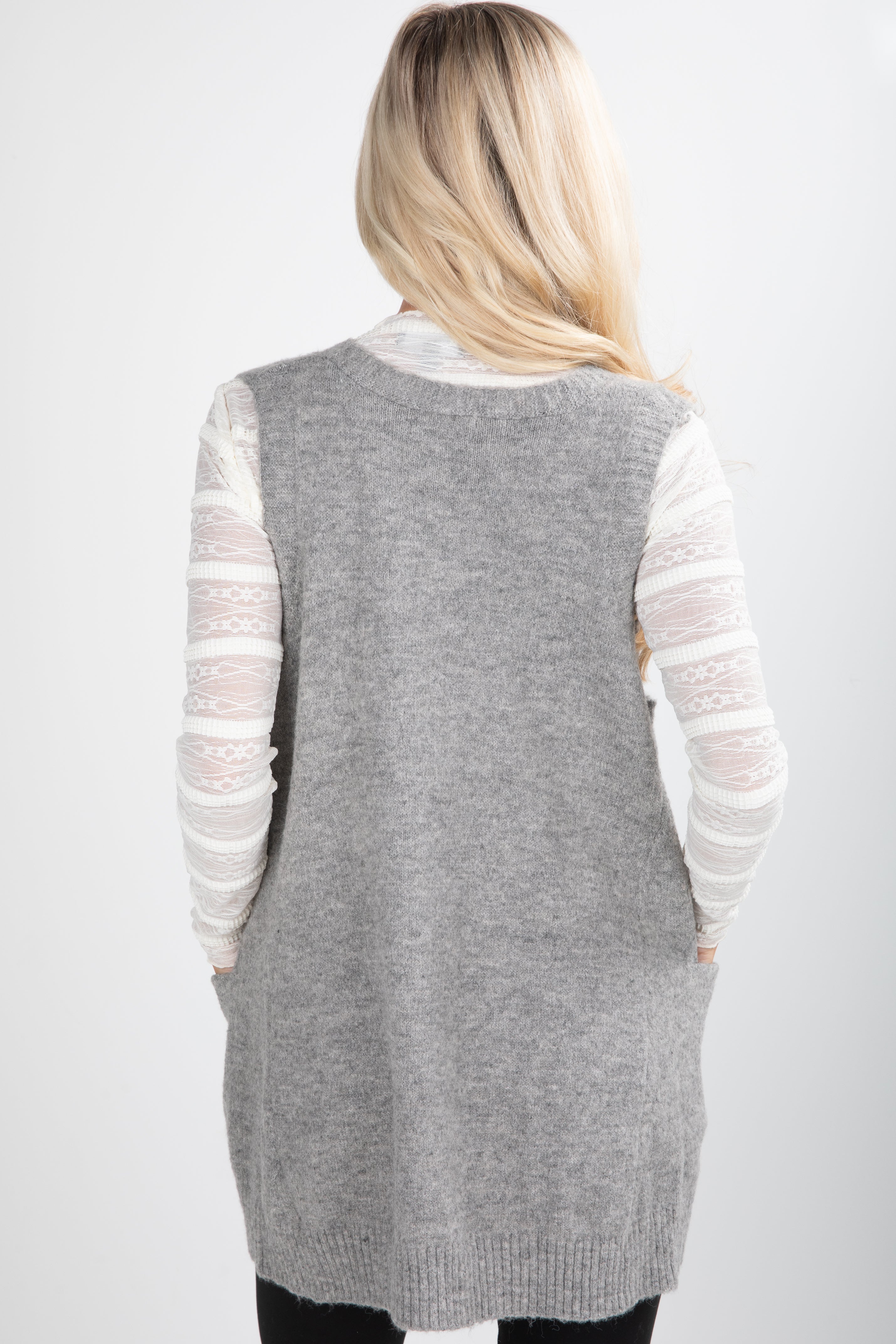 Person wearing a gray cardigan over a white long-sleeve shirt on a white background