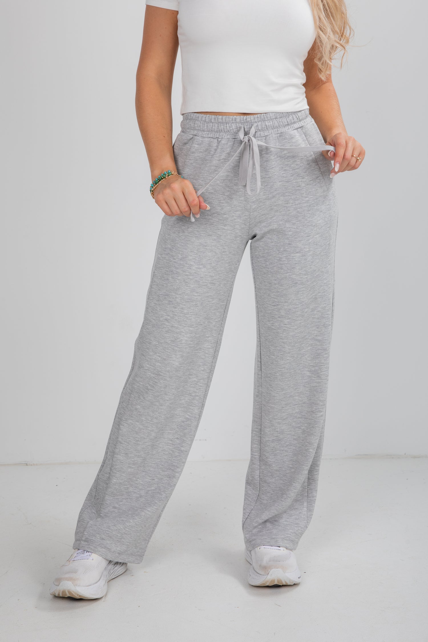 Person wearing gray sweatpants and a white top on a plain background
