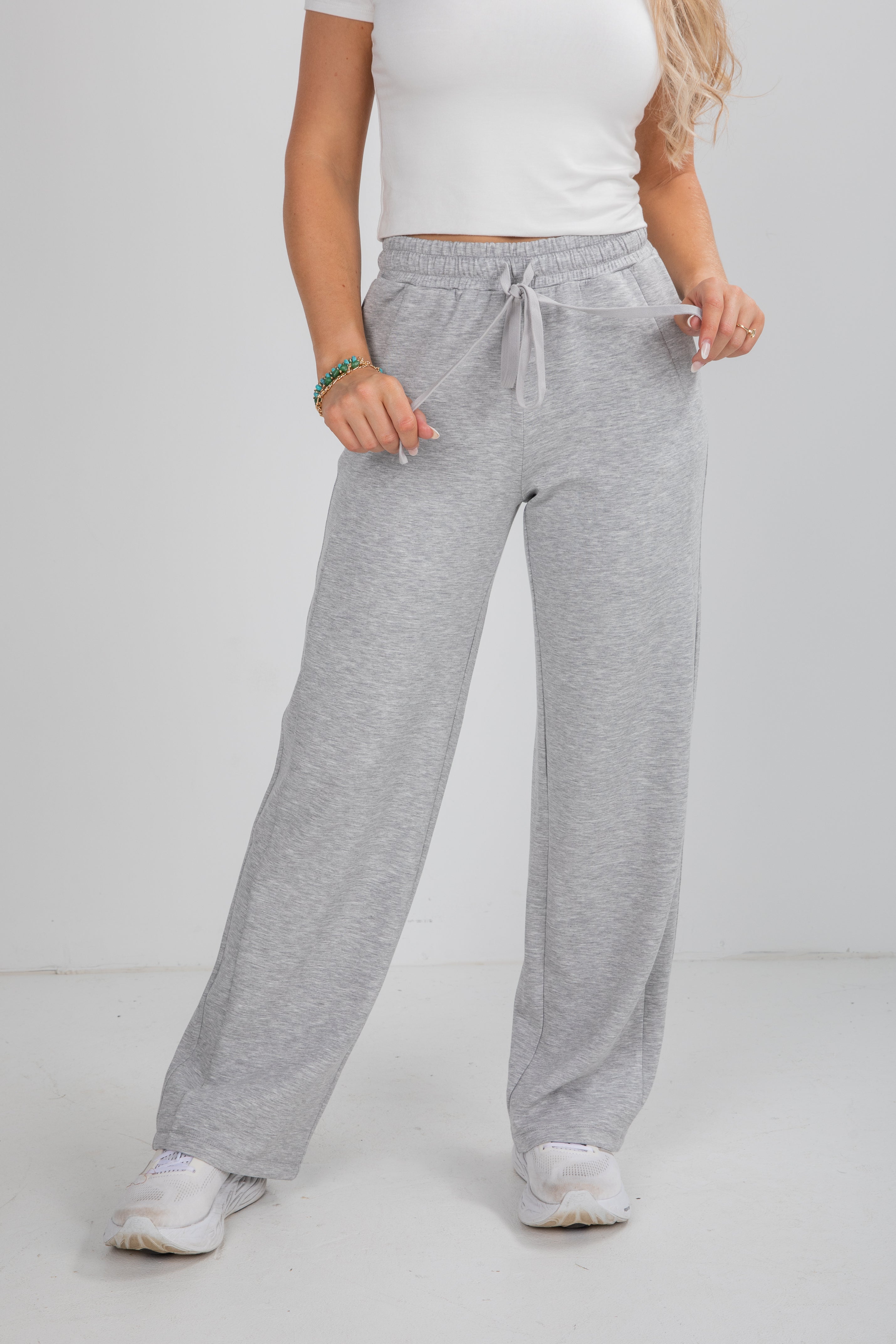 Person wearing gray sweatpants and a white top on a plain background