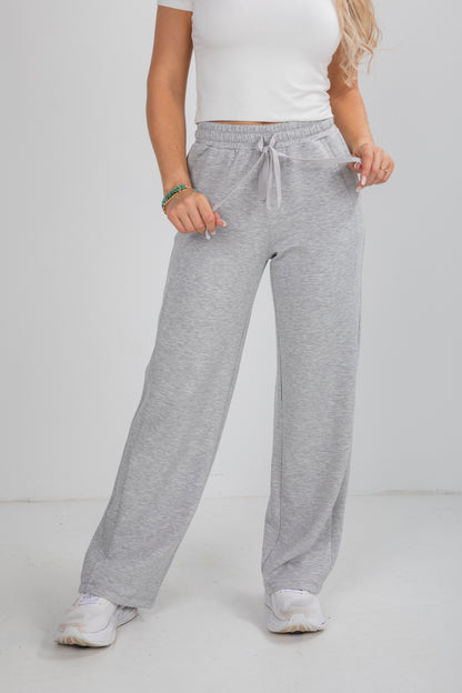 Person wearing gray sweatpants and a white top on a plain background