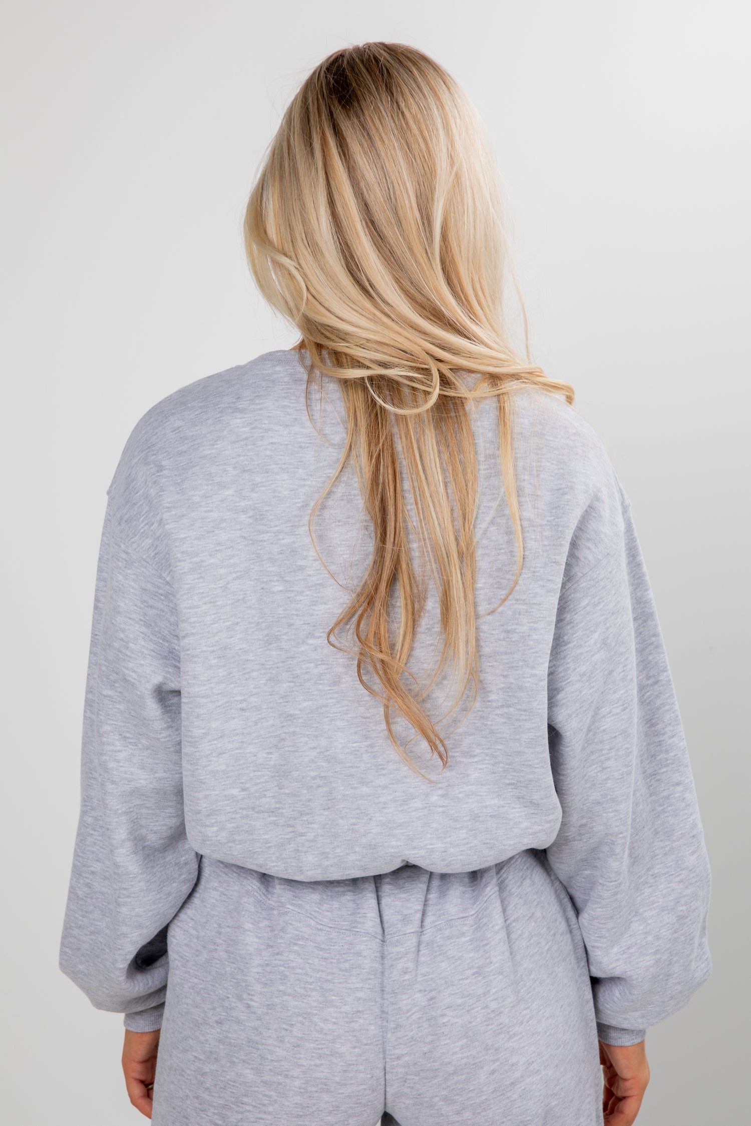Person wearing a gray tracksuit with long blonde hair on a plain background