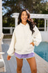 Woman wearing a white hoodie and purple shorts standing by a pool.