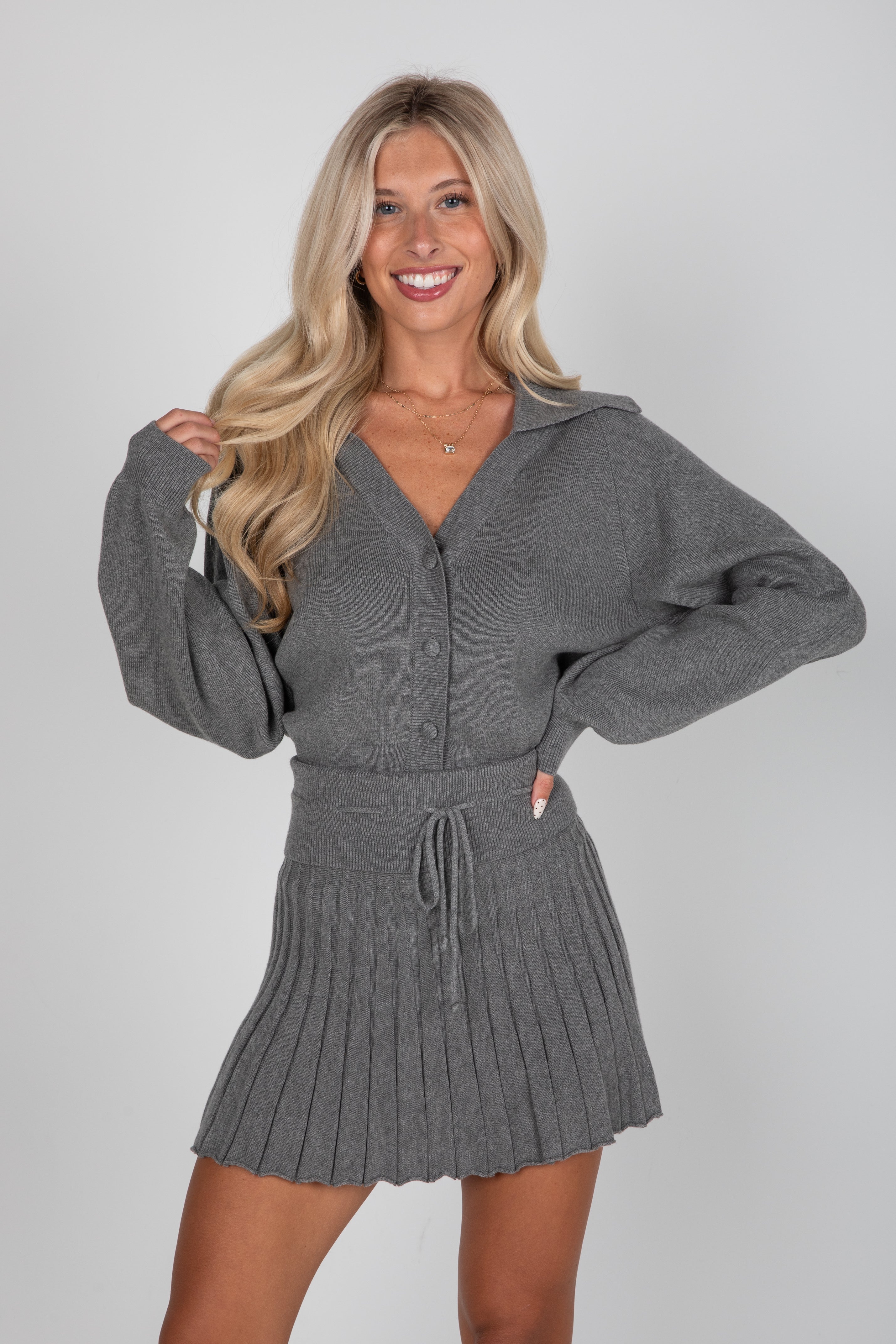 Woman wearing a gray sweater and skirt set on a plain background
