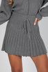 Gray pleated skirt worn with a matching gray sweater on a plain background