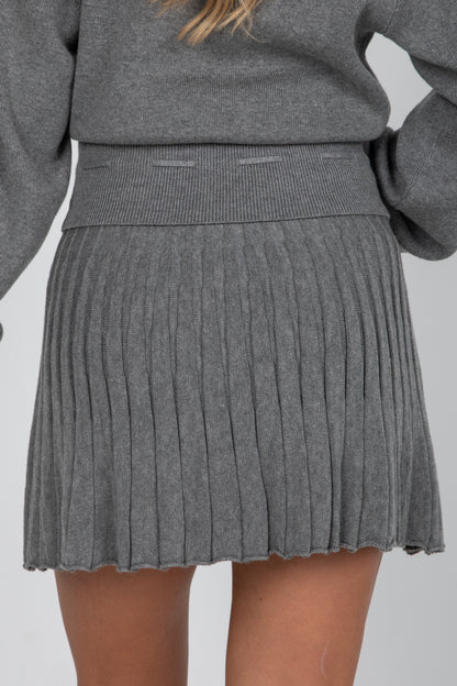 Person wearing a gray pleated skirt and sweater on a plain background