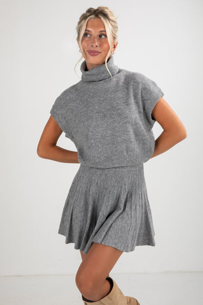 Woman wearing a gray knit dress with a cowl neck on a white background