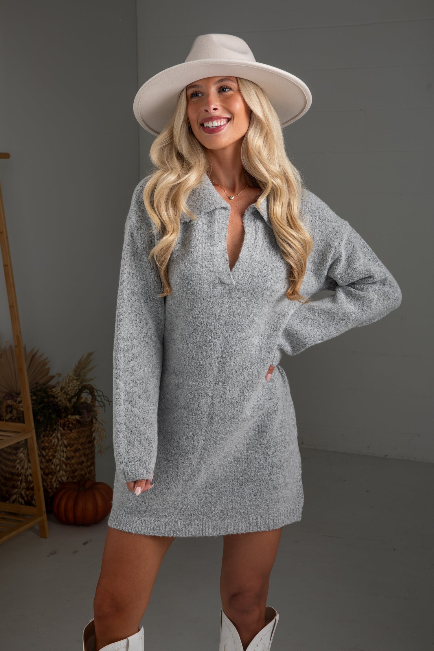 Woman wearing a gray dress with a cut-out design, white hat, and white boots in a neutral setting.