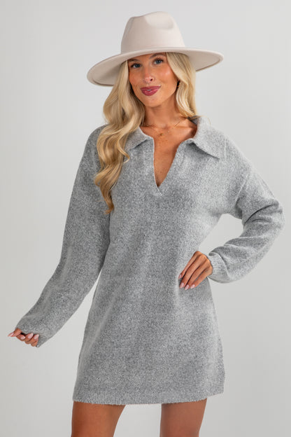 Woman wearing a gray sweater dress and beige hat on a plain background